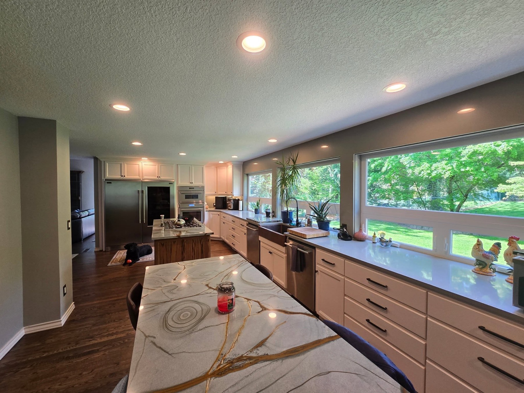 A bright, freshly cleaned kitchen with a marble island and big windows onto a green yard